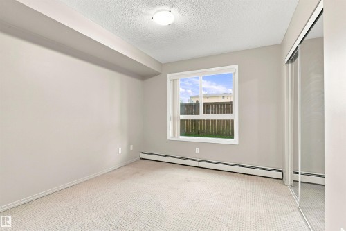 Neutral wall tones with carpet flooring, a large window, and mirrored sliding closet doors - #117 17011 67 Av Nw, Edmonton, AB - Indoor Photo Showing Other Room