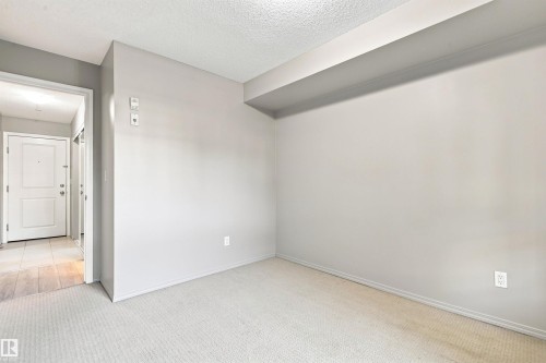 Light gray wall paint, textured ceiling, light-toned carpeting, and a contrasting entry door with hardware - #117 17011 67 Av Nw, Edmonton, AB - Indoor Photo Showing Other Room