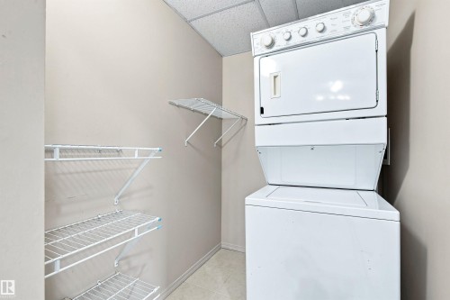 Laundry area with stacked washer and dryer, accompanied by wire shelving - #117 17011 67 Av Nw, Edmonton, AB - Indoor Photo Showing Laundry Room