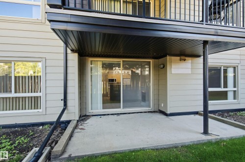 Ground-level patio with concrete surface, direct exterior access via sliding glass door, and overhead balcony for shelter - #117 17011 67 Av Nw, Edmonton, AB - Outdoor With Exterior