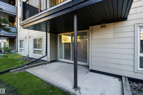 Ground-level patio with concrete slab, sliding glass door access, and an overhead balcony - #117 17011 67 Av Nw, Edmonton, AB - Outdoor With Exterior