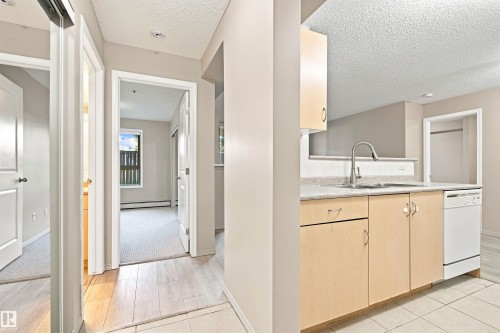 Kitchen featuring light wood-finish cabinetry, a stainless steel sink with a gooseneck faucet, light countertop, and a white dishwasher - #117 17011 67 Av Nw, Edmonton, AB - Indoor Photo Showing Kitchen