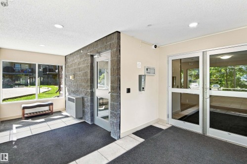 Entryway featuring large windows, glass-paneled doors, recessed lighting, and a textured stone-finish wall - #117 17011 67 Av Nw, Edmonton, AB -  Photo Showing Other Room