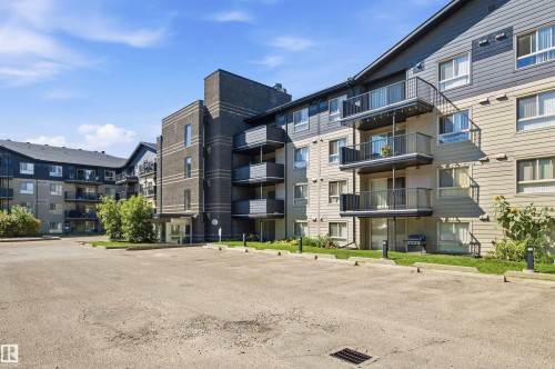 Multi-story building featuring brick and siding exterior, multiple balconies with metal railings, and a paved parking area - #117 17011 67 Av Nw, Edmonton, AB - Outdoor With Facade