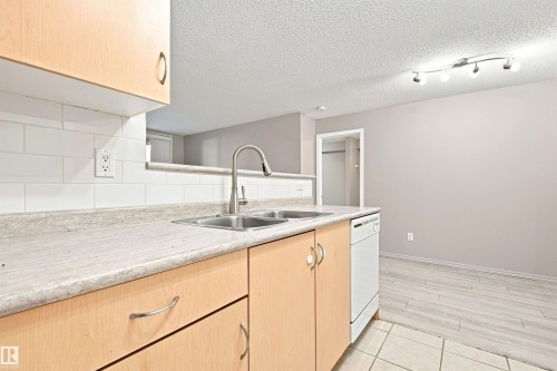 Kitchen featuring light wood-finish cabinetry, a dual basin stainless steel sink with a gooseneck faucet, white subway tile backsplash, and a white built-in dishwasher - #117 17011 67 Av Nw, Edmonton, AB - Indoor Photo Showing Kitchen With Double Sink