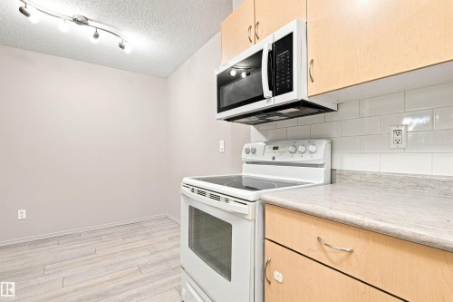 Light wood-finish cabinetry, white subway tile backsplash, light wood-finish flooring, and track lighting - #117 17011 67 Av Nw, Edmonton, AB - Indoor Photo Showing Kitchen
