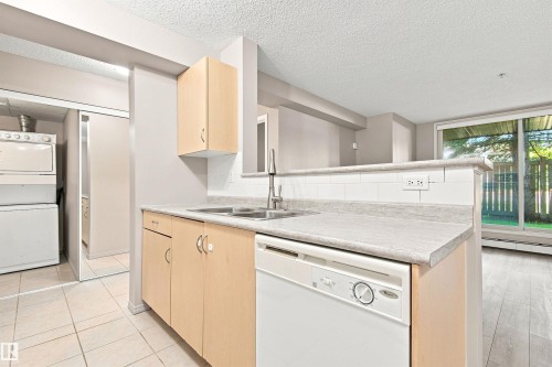 Kitchen with light wood-finish cabinetry, light-colored countertops, and a white tile backsplash - #117 17011 67 Av Nw, Edmonton, AB - Indoor Photo Showing Kitchen With Double Sink
