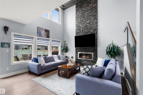Vaulted ceiling with high windows, stone-faced fireplace with a gas insert, wood-finish flooring, glass panel railing - 16327 17 Avenue Sw, Edmonton, AB 