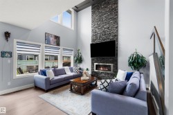 Vaulted ceiling with high windows, stone-faced fireplace with a gas insert, wood-finish flooring, glass panel railing - 
