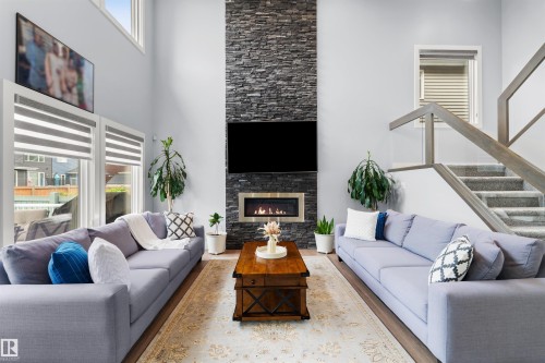 Vaulted ceiling, stone-clad fireplace with built-in insert, large windows, wood-finish flooring, and a staircase with glass panel railing - 16327 17 Avenue Sw, Edmonton, AB 