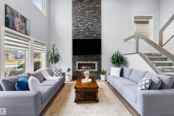 Vaulted ceiling, stone-clad fireplace with built-in insert, large windows, wood-finish flooring, and a staircase with glass panel railing - 