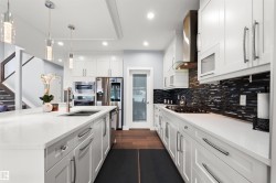 Kitchen featuring white cabinetry, stainless steel appliances, dark wood-finish flooring, white countertops, and a dark mosaic tile backsplash - 