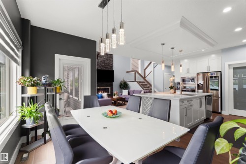 Open-concept living area with a contemporary kitchen island, stainless steel appliances, and a stone-clad fireplace - 16327 17 Avenue Sw, Edmonton, AB 