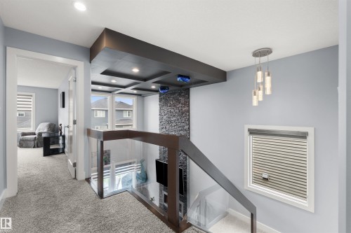 Modern glass and wood railing, recessed lighting, coffered ceiling detail, stacked stone accent wall, and contemporary pendant light fixture - 16327 17 Avenue Sw, Edmonton, AB 