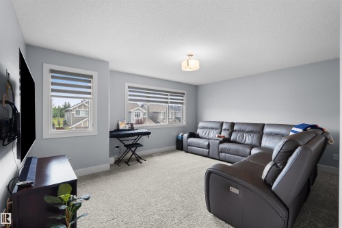 Carpeted room featuring multiple windows with blinds, a wall-mounted light fixture, and light-toned wall paint - 16327 17 Avenue Sw, Edmonton, AB 