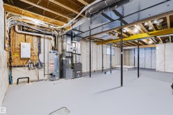 Unfinished basement with exposed ceiling joists, painted concrete flooring, a water heater, and a furnace unit - 