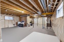 Unfinished lower level featuring exposed wood joists, structural support beams, concrete flooring, and multiple windows - 