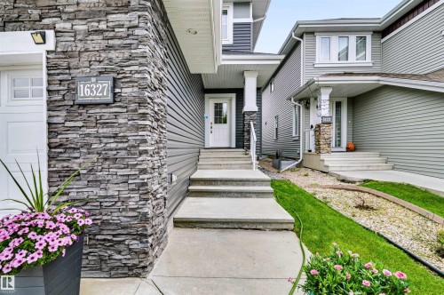Stone veneer accents, white front door, covered entry, concrete walkway, and gray siding - 16327 17 Avenue Sw, Edmonton, AB 
