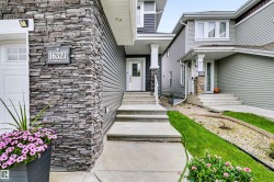 Stone veneer accents, white front door, covered entry, concrete walkway, and gray siding - 