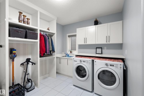 White cabinetry with shaker-style doors, integrated laundry sink, built-in shelving, and dedicated hanging rod - 16327 17 Avenue Sw, Edmonton, AB 