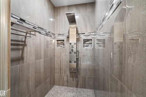 Tiled shower enclosure featuring a multi-function shower panel, recessed niches with mosaic tile accents, and a mosaic tiled shower floor - 16327 17 Avenue Sw, Edmonton, AB 