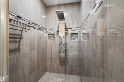 Tiled shower enclosure featuring a multi-function shower panel, recessed niches with mosaic tile accents, and a mosaic tiled shower floor - 