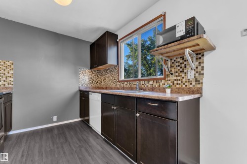 Kitchen featuring dark wood-finish cabinetry, mosaic tile backsplash, solid surface countertops, and wood-finish flooring - 3425 48 Street Nw, Edmonton, AB - Indoor
