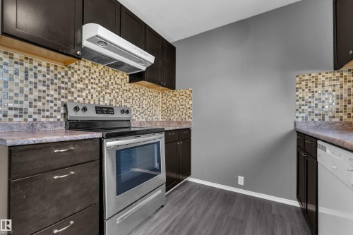 Dark wood-finish cabinetry, mosaic tile backsplash, stainless steel electric range, white dishwasher, and wood-finish flooring - 3425 48 Street Nw, Edmonton, AB - Indoor Photo Showing Kitchen