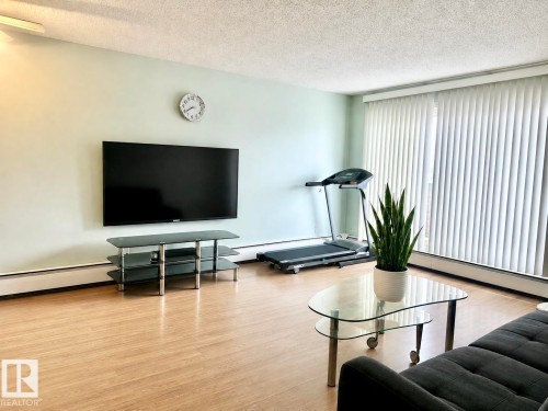 Wood-finish flooring, light-toned wall paint, and vertical window blinds - #106 10620 104 St Nw, Edmonton, AB - Indoor Photo Showing Living Room
