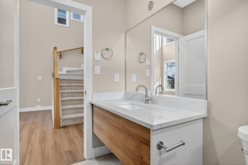 Wall-mounted vanity with wood-finish cabinet and white countertop, undermount sink with chrome-finish faucet, and large frameless mirror - 9736 73 Avenue Nw, Edmonton, AB 