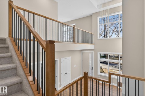 Two-story entry with a wood-finish staircase and black balusters, featuring a large multi-pane window and a modern linear chandelier - 9736 73 Avenue Nw, Edmonton, AB 