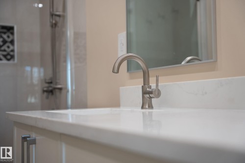 Integrated vanity sink with a light-colored countertop, brushed nickel faucet, and a wall-mounted mirror - 9736 73 Avenue Nw, Edmonton, AB 