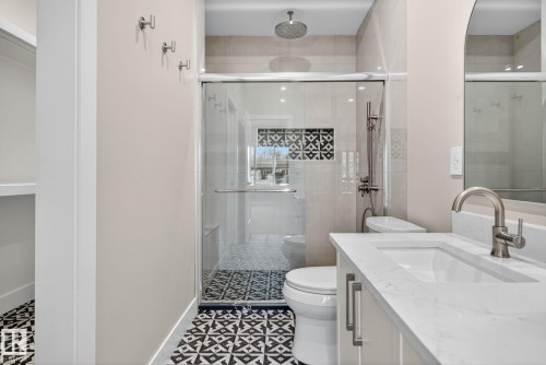 Patterned floor tiling, glass-enclosed shower, rain shower head, built-in shower niche with decorative tiling, and a vanity with an integrated sink and brushed nickel faucet - 9736 73 Avenue Nw, Edmonton, AB 