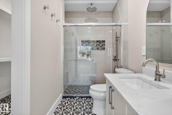 Patterned floor tiling, glass-enclosed shower, rain shower head, built-in shower niche with decorative tiling, and a vanity with an integrated sink and brushed nickel faucet - 