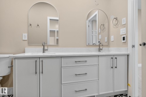 Dual arched mirrors, dual undermount sinks, white quartz countertop, custom cabinetry with brushed nickel hardware, and patterned floor tile - 9736 73 Avenue Nw, Edmonton, AB 