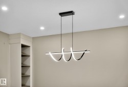 Modern linear chandelier with integrated lighting, recessed ceiling lights, built-in shelving, and neutral wall tones - 