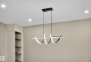 Modern linear chandelier with integrated lighting, recessed ceiling lights, built-in shelving, and neutral wall tones - 9736 73 Avenue Nw, Edmonton, AB 