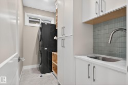 Laundry area featuring stacked appliances, white cabinetry with silver hardware, a utility sink with a gooseneck faucet, and a tiled backsplash - 