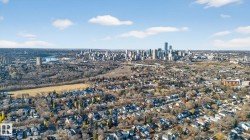 Urban skyline visible in the distance, featuring multiple high-rise structures, surrounded by established residential areas with varied rooflines and a significant expanse of natural tree cover - 