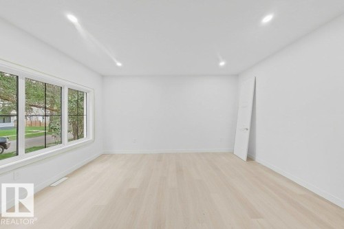 Bright, light-filled room showcasing refinished wood-finish flooring, recessed ceiling lighting, and expansive multi-pane windows framing outdoor landscape views - 9736 73 Avenue Nw, Edmonton, AB - Indoor Photo Showing Other Room