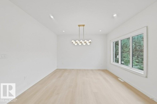 White walls, recessed lighting, wood-finish flooring, and a modern linear chandelier - 9736 73 Avenue Nw, Edmonton, AB - Indoor Photo Showing Other Room