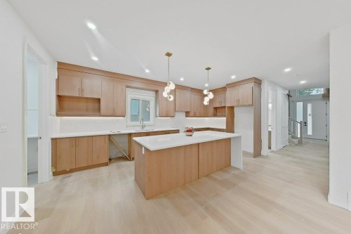 Kitchen featuring a central island, light wood-finish cabinetry, solid surface countertops, and modern pendant lighting - 9736 73 Avenue Nw, Edmonton, AB - Indoor Photo Showing Kitchen