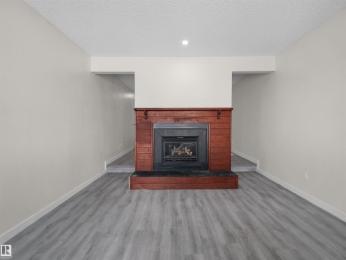 Wood-finish flooring with a gas fireplace featuring a wood surround and black hearth - #47 1904 48 St Nw, Edmonton, AB - Indoor Photo Showing Living Room With Fireplace