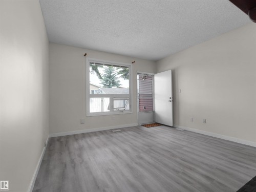 Light gray wood-finish flooring, white walls, white trim, and a white entry door with a storm door - #47 1904 48 St Nw, Edmonton, AB - Indoor Photo Showing Other Room