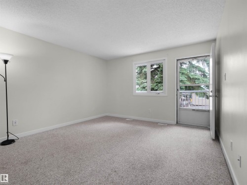 Neutral wall color, light-toned carpet, window with exterior landscaping, and an exterior door with a screen - #47 1904 48 St Nw, Edmonton, AB - Indoor Photo Showing Other Room