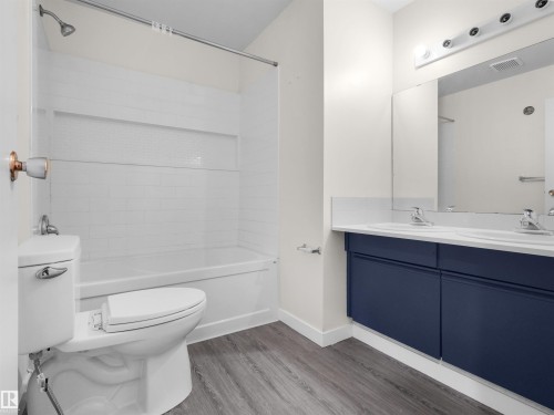 Wood-finish flooring, white subway tile shower surround with integrated niche, white porcelain tub, dual vanity with blue cabinetry, and white countertop - #47 1904 48 St Nw, Edmonton, AB - Indoor Photo Showing Bathroom