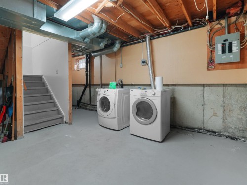 Dedicated laundry area with a washer and dryer, exposed ceiling joists, concrete foundation walls, and a finished staircase - #47 1904 48 St Nw, Edmonton, AB - Indoor Photo Showing Laundry Room