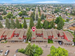 Townhouse community with red-sided units, individual carport parking, and mature evergreen trees - 