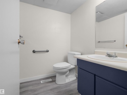 Bathroom featuring a vanity with a dark blue cabinet, an integrated sink, a wall-mounted mirror, a toilet, and wood-finish flooring - #47 1904 48 St Nw, Edmonton, AB - Indoor Photo Showing Bathroom