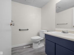 Bathroom featuring a vanity with a dark blue cabinet, an integrated sink, a wall-mounted mirror, a toilet, and wood-finish flooring - 